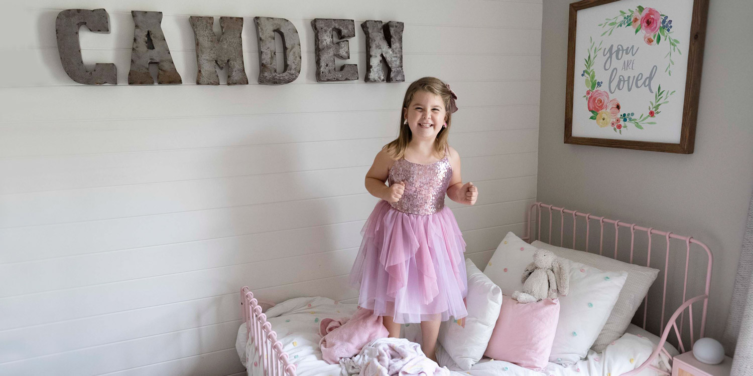 Camden smiles as she bounces on her bed. Letters on the wall spell her name.