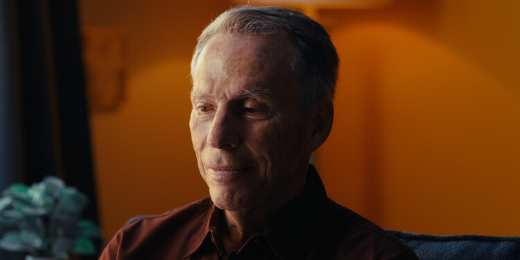 A portrait of Joe Mesiano sitting in a room with a orange background