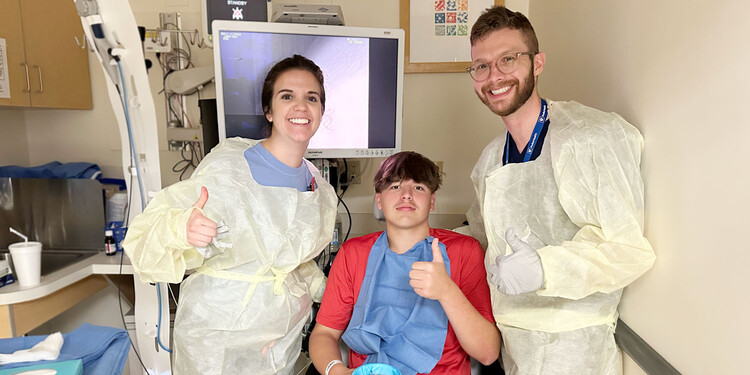 Two medical team members stand beside Richard Best in a procedure room. They are all giving a thumbs up.