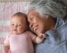 A grandma smiles at her grandchild as they cuddle on a blanket on the floor