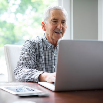 An elderly man works on a laptop